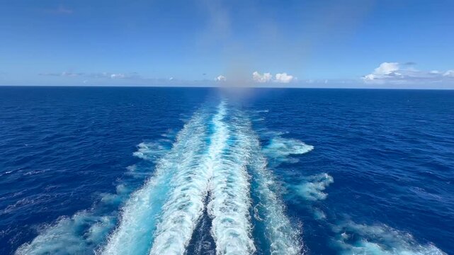 Unedited footage from 14th deck stern of a cruise liner crossing the Atlantic. Sunny, windless day, clear skies, and a flat calm ocean in light blue. Two propeller wakes and a foamy keel trail stretch