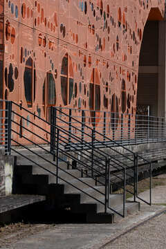 Black stairs rise along a brick facade, where architecture, handrail, steps, exterior urban pattern and walkway cut across a warm wall