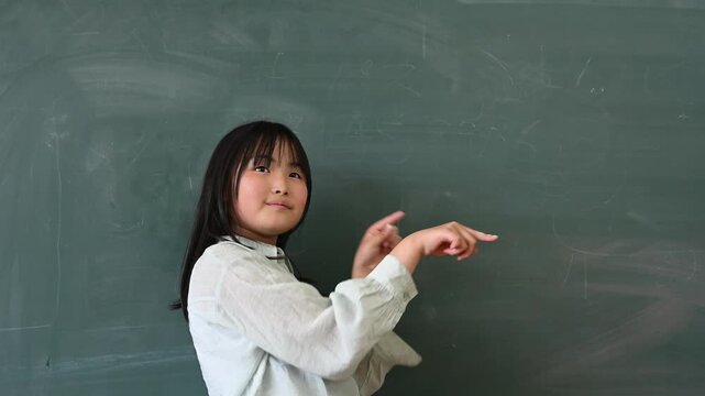 教室の黒板の前で笑顔で指差しをする高学年の女子小学生