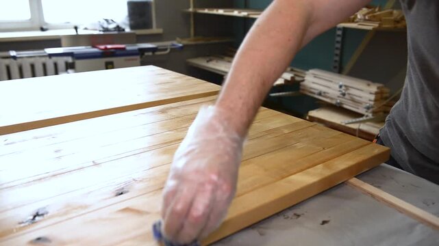Hand applying wood protection oil on boards with rags. Hand applying wood protection piece in gold color with rags, indor. Impregnation of wood and coating with oil