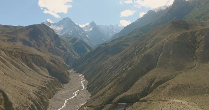 Drone glides in slow motion to unveil a sweeping, rugged valley, himalayas and deserted riverbed in Mustang, Nepal.