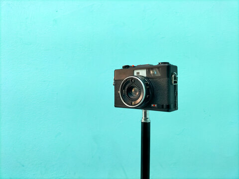Vintage film camera on a monopod against a solid turquoise wall background.