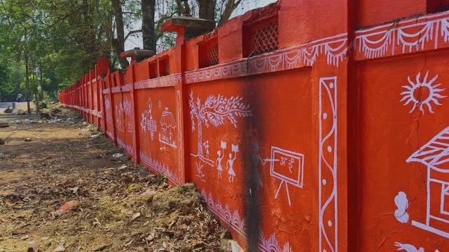 Cinematic slow tracking view of long terracotta red wall decorated with traditional white Warli tribal paintings showing rural life cultural figures huts trees and folk art from India