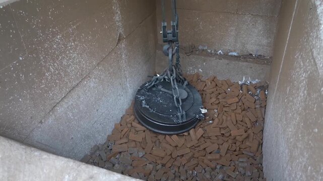 Electromagnetic crane lowering into concrete bin to pick up steel billets for furnace loading