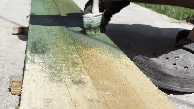 Person Painting Wooden Plank with Brush Outdoors in Daylight