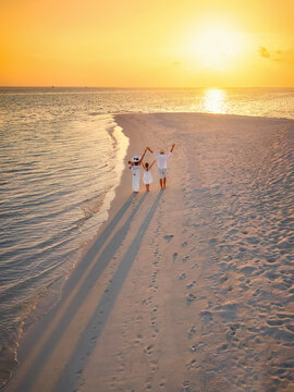 Elevated view of a happy family in white summer clothing walking a tropical beach in the Maldives islands during sunset time