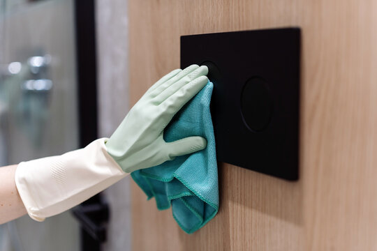 Woman cleaning water flush button with cloth in modern restroom