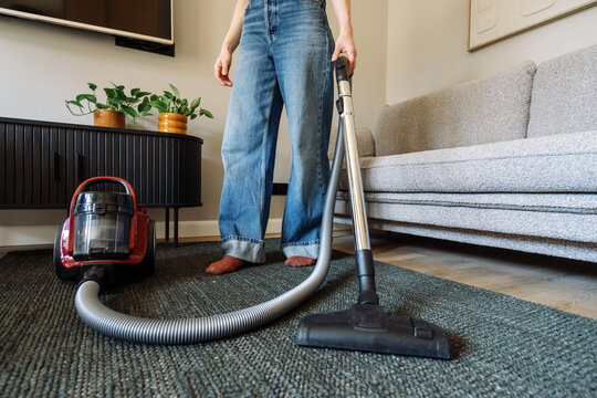 Woman cleans floor with vacuum cleaner in modern apartment living room