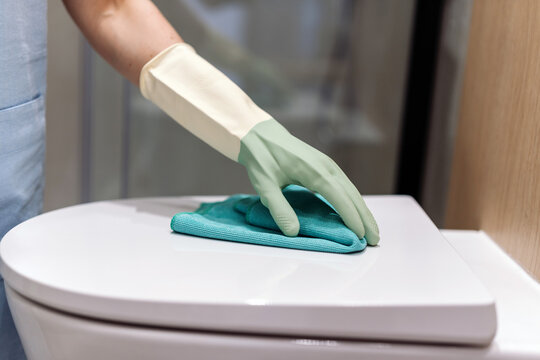 Woman cleans toilet lid in modern restroom using protective gloves and cloth