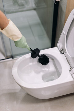 Woman cleans toilet bowl in modern restroom, using brush