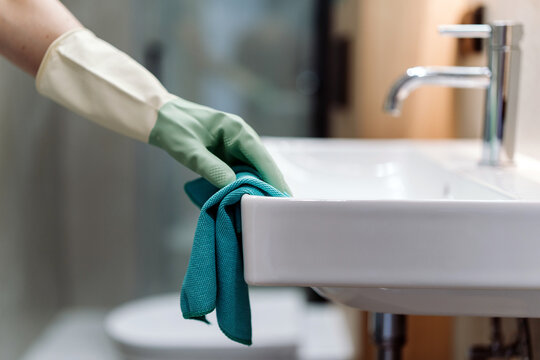 Woman cleaning bathroom sink with gloves in a modern apartment