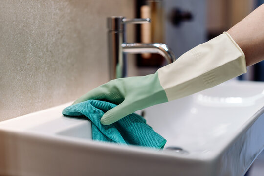 Woman cleaning bathroom sink in modern apartment with gloves on her hand