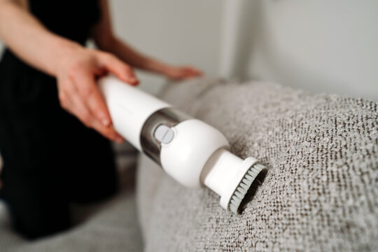 Woman uses cordless vacuum cleaner to clean couch in modern living room