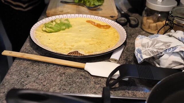 Cooking process: hands place avocado and sauce on omelet