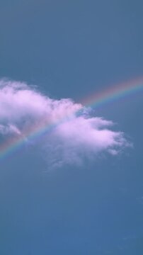 Vibrant vertical portrait rainbow cutting through a clear blue sky with few minimal soft clouds.