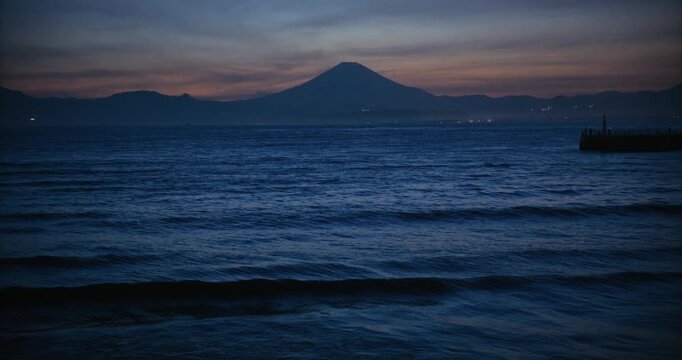 Majestic waves rolling onto Japanese shore with silhouette of hill in distance