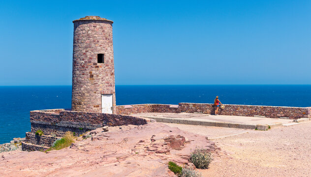 Woman traveler standing by the historic pink sandstone foghorn tower at Cap d'Erquy, Brittany, France