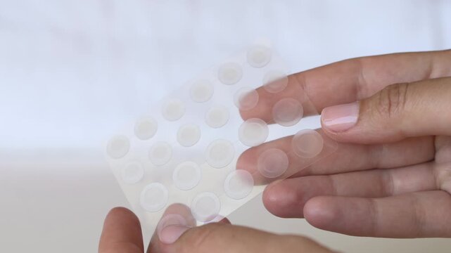 Hands holding sheet of hydrocolloid acne patches on soft neutral background. Popular Korean skincare inspired beauty product for blemish care, spot treatment and clear skin routines.