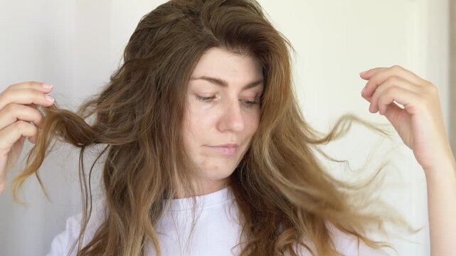 Close-up of woman inspecting weak damaged hair and breakage problems at home. Commercial concept for trichology consultation, anti hair loss therapy and professional hair restoration.