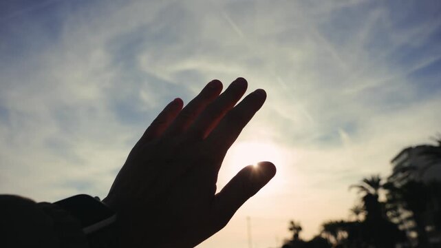 Hand reaching toward the sky with sunlight shining through the fingers. Freedom, hope, inspiration and connection with nature concept. High quality 4k footage