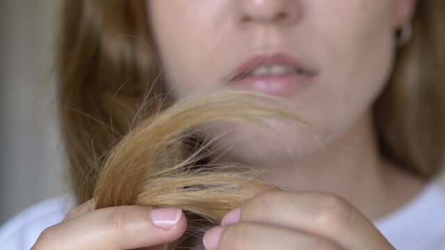 Close-up of woman checking dry hair tips after sun and heat exposure. Commercial concept for post summer hair recovery, UV protection products and nourishing haircare cosmetics