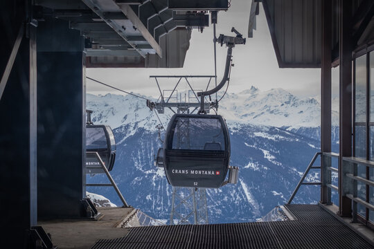 Crans-Montana, Switzerland - February 1, 2026: Gondola leaving Les Violettes funicular top station with scenic view over Rhone Valley against cloudy sky