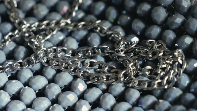 Close-up of silver chain lying on a textured beaded surface. Fashion accessory, jewelry detail and luxury design concept. High quality 4k footage