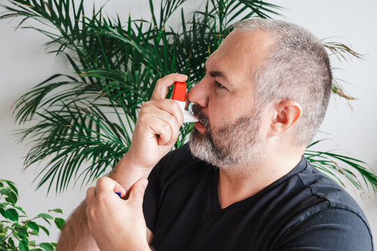 Mature man uses a red asthma inhaler at home illustrating respiratory treatment breathing relief and chronic condition management in a warm everyday healthcare scene.