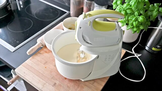 An electric stand mixer blends smooth pale yellow cake batter in a bowl in a modern marble kitchen baking a homemade sponge cake from scratch.
