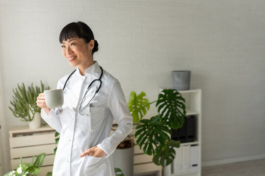 Happy doctor taking a moment to relax with a hot drink in clinic. Workplace wellness, healthcare profession and positive mindset concept