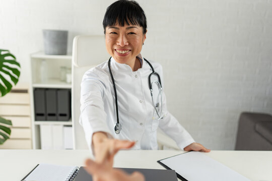 Friendly female doctor reaching out for a handshake in modern clinic. Patient welcome, trust, healthcare consultation and positive medical experience concept