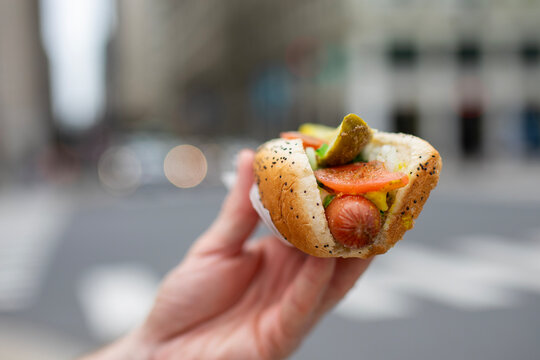 Close-up of hand holding traditional Chicago style hot dog on street city background. Fast food, american cuisine, street food culture and summer lunch concept.