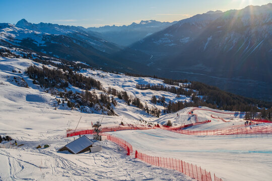 Sunrise over the Rhone Valley with snow-covered mountains and part of the men's racecourse of the 2027 Alpine World Ski Championchips in Crans-Montana, Switzerland against blue sky