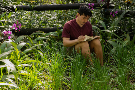 Freckled young man sitting outdoors enjoying reading a book in a natural setting. Leisure, relaxation, tranquility, and connection with nature concept
