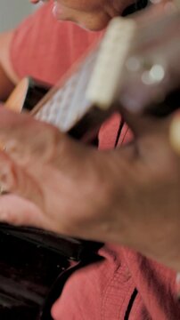 Vertical video: Pulling back revealing woman strumming guitar and singing at home with headphones