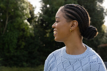 African American woman standing in park in light blue sweater gold hoops braided bun, copy space © wavebreak3