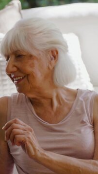 Vertical video: Turning, senior woman in pink top giving thumbs-up, waving on sofa, tablet calling