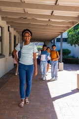 Fototapeta premium African American students walking under wooden roof on brick walkway at school carrying backpacks