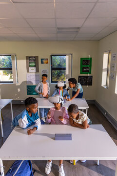 African American children gathering around two white tables at school, one child wearing VR headset