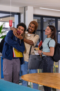Diverse students gathering in modern campus common area, sharing smartphone and notebooks
