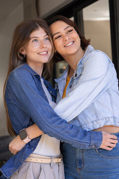 Diverse female partners embracing and smiling at doorway in denim near sliding door with smartwatch