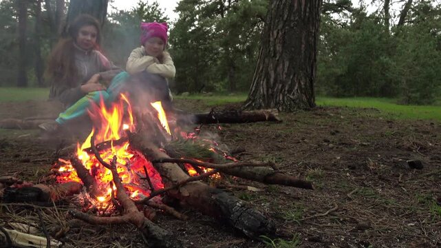 Two little girls are sitting by fire in forest