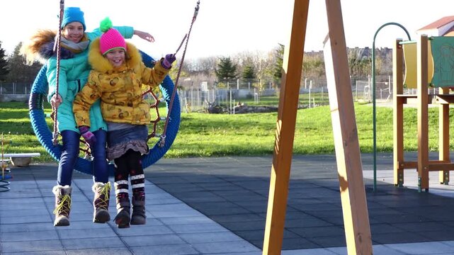 two beautiful girls ride a round swing in the autumn zoo