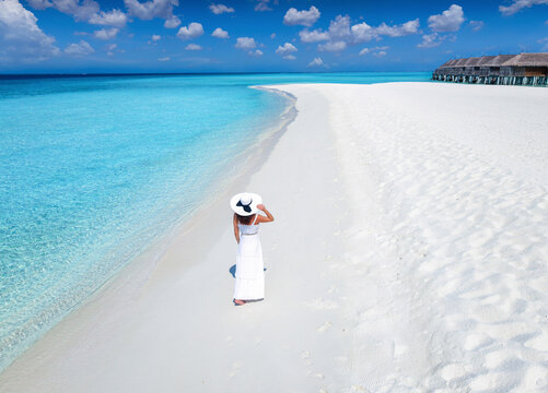 A beautiful woman in a white dress stands on a tropical beach with turquoise sea in the Maldives Islands, Indian Ocean