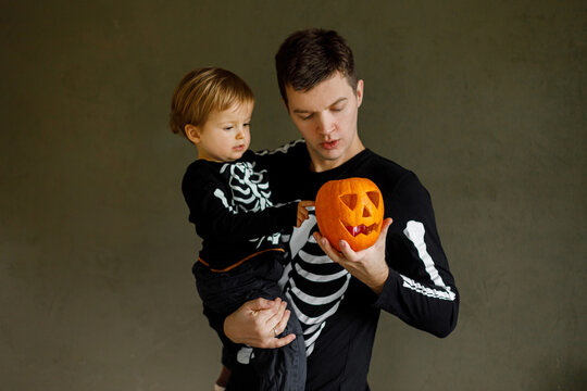 Happy Halloween. Father with child standing with carved halloween pumpkin and trick or treating on dark background. Dad and son in skeleton costumes together