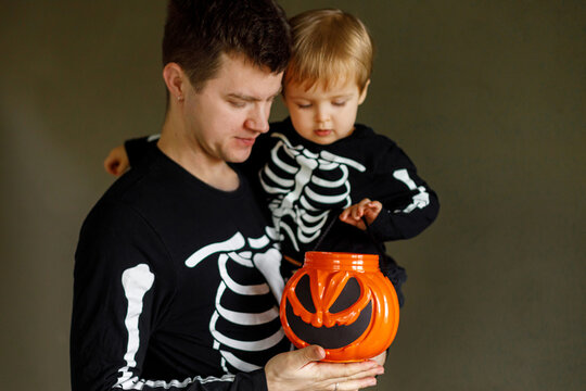 Happy Halloween. Father with child standing with carved halloween bucket and trick or treating on dark background. Dad and son in skeleton costumes together