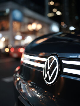 Volkswagen-Logo an der Front eines Fahrzeugs bei Nacht in urbaner Umgebung. Editorial-Motiv f&uuml;r Automobilindustrie, Markenwahrnehmung, Mobilit&auml;t, Fahrzeugdesign und Stadtverkehr.