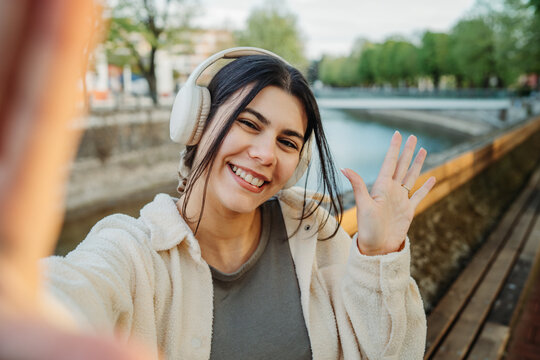 Woman with headphones waving hand during selfie video call