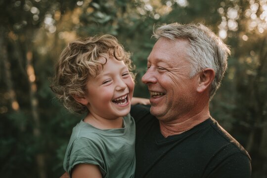 Father's Day. Cheerful older father,  cradling laughing baby against chest, gray in hair, black shirt, park backdrop. Late parenthood, senior man dad, tender natural portrait, older age fatherhood.