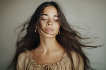 Naklejka premium Beautiful Spanish or hispanic woman with long hair blowing in wind, beige dress, neutral background, close-up face portrait. Soft lighting, shallow depth, elegant movement. Hairstyle ad.